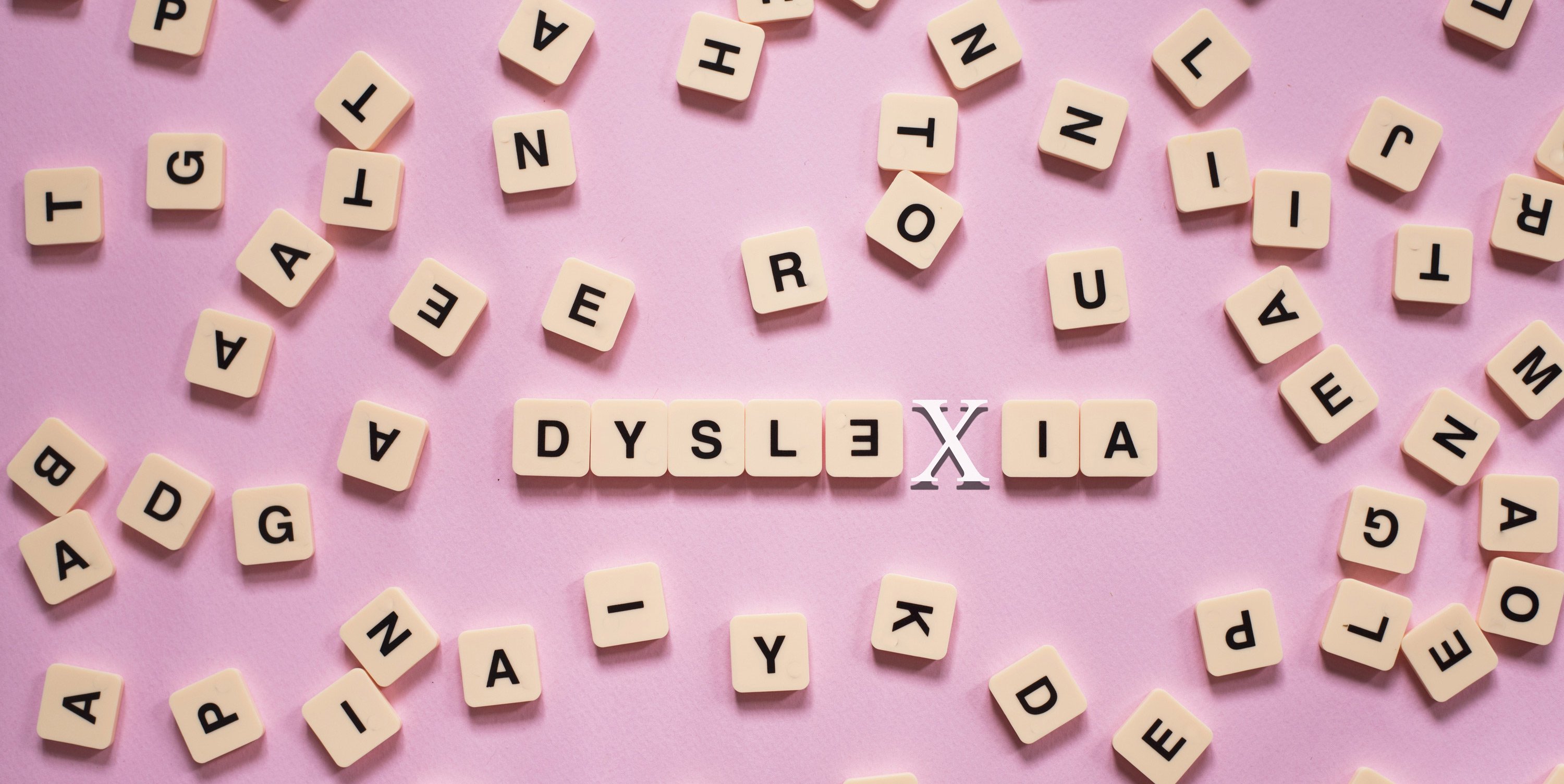 Letter tiles spilled on a pink table that spell out dyslexia